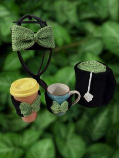 two coffee mugs and a hat are hanging from a string with green leaves in the background