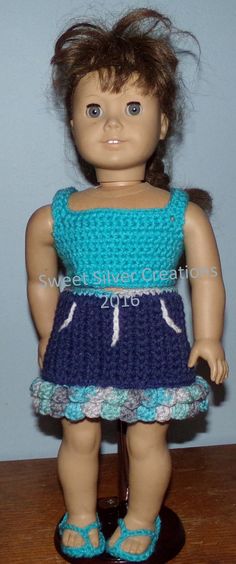 a doll is wearing a blue dress and sandals on a table with a wall in the background