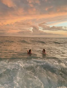 two people swimming in the ocean at sunset