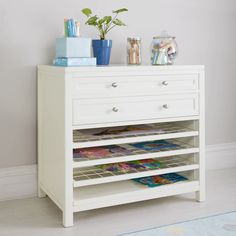 a white dresser with magazines and plants on top