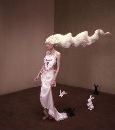 a woman with long white hair standing next to rabbits