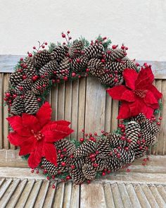 a christmas wreath with poinsettis and pine cones on a wooden table top