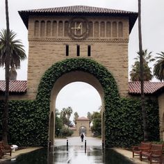 an archway in the middle of a courtyard with benches and palm trees on either side