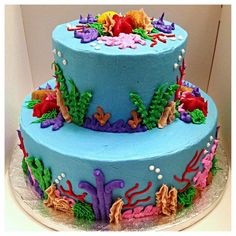 a three tiered blue cake decorated with sea animals and corals on the side