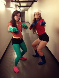 two women dressed in costumes standing next to each other on a long hallway with one pointing at the camera