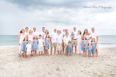 a large family poses for a photo on the beach in front of an ocean and cloudy sky