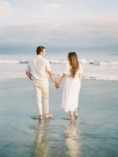 a man and woman holding hands while standing in the water at the ocean's edge