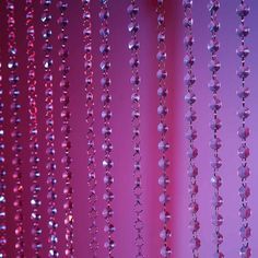 some beads are hanging from the side of a window in front of a pink wall