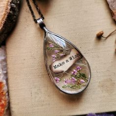 a glass tear shaped necklace with flowers on it and the words make a wish written in black ink