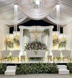 a stage set up for a wedding with white chairs and greenery on the side