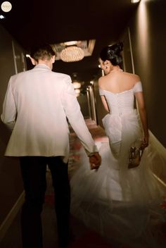 a man and woman dressed in formal wear walking down a hallway holding hands with each other