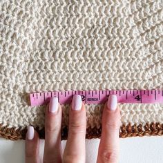 a woman's hands holding a ruler on top of a piece of crochet