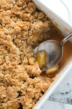 a close up of a spoon in a casserole dish filled with fruit and oatmeal