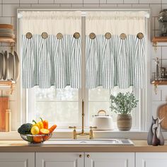 a kitchen with white cabinets and green striped valances on the windowsills, along with various fruits and vegetables in a bowl