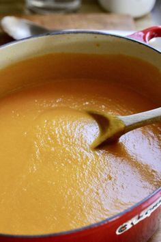 a red pot filled with soup on top of a wooden table