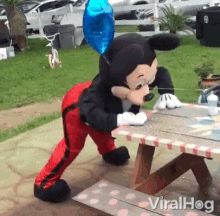 a mickey mouse sitting at a picnic table with balloons attached to it's ears