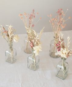 three clear vases with dried flowers in them on a white tableclothed surface