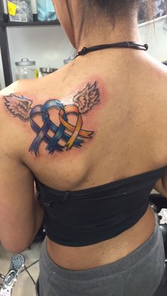 the back of a woman's shoulder with an angel and ribbon tattoo on it