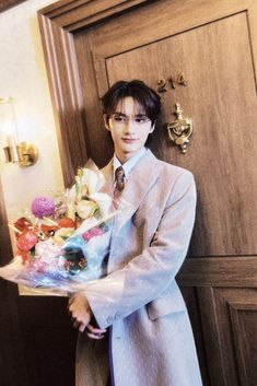 a man in a gray suit holding a bouquet of flowers next to a wooden door