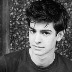 black and white photo of a young man in front of a wall with leaves on it