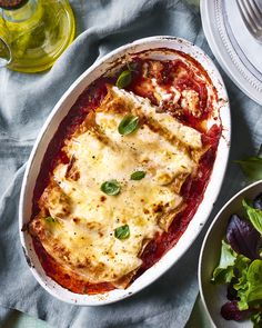 a casserole dish with meat, cheese and sauce next to salad on a table