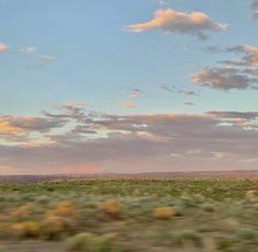 the sky is filled with clouds and there are green grass in the foreground, as seen from a moving train