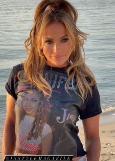 a woman standing on top of a sandy beach next to the ocean in front of a cell phone