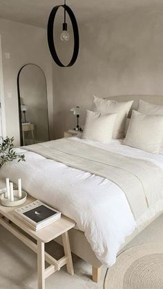 a bed with white sheets and pillows next to a small table on the floor in front of a mirror