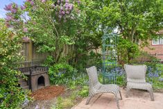 two wicker chairs sitting in the middle of a garden next to a fire place