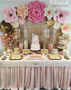 a table topped with lots of cakes and desserts next to a wall covered in paper flowers