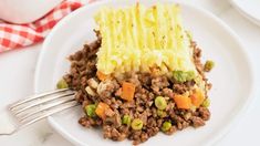 a white plate topped with meat and veggies next to a red checkered napkin