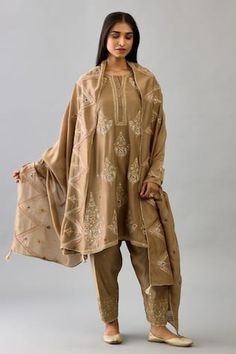 Taupe silk chanderi kalidar phiran style kurta with all over floral, vintage motifs, multi color silk thread, dori, zari and sequin embroidery. Paired with embroidered narrow salwar and chevron bordered dupatta. Components: 3 Pattern: Embroidered Type Of Work: Zari, Dori, Silk Thread, Sequin and Gota Work Neckline: Round Sleeve Type: Three Quarter Sleeves Fabric: Silk Chanderi Color: Brown Other Details:  Cut work hem details Side pockets Panelled kurta Gota lace work border details Tasselled du Transitional Chanderi Unstitched Suit With Traditional Drape, Festive Unstitched Raw Silk Suit With Naqshi, Silk Lawn Suit With Zari Work In Traditional Drape, Chanderi Salwar Kameez With Naqshi In Traditional Drape, Cotton Silk Dupatta With Naqshi In Traditional Drape, Raw Silk Unstitched Suit With Naqshi For Festivals, Traditional Drape Dupatta In Cotton Silk With Naqshi, Chanderi Anarkali Set With Naqshi In Traditional Drape, Anarkali Tussar Silk Lawn Suit Designer Wear