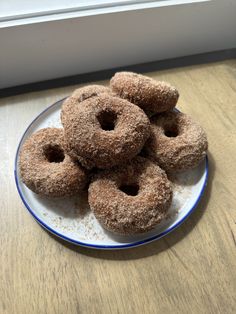 a plate full of sugared donuts sitting on a wooden table next to a window