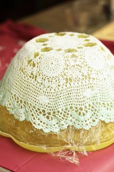 a white hat sitting on top of a pink tablecloth covered plate with doily