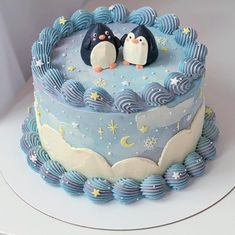 there is a cake with two penguins on top and blue icing around the edges