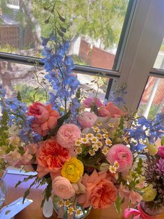 a vase filled with lots of colorful flowers on top of a table next to a window