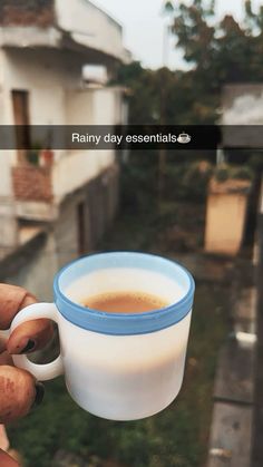 a hand holding a cup of coffee in front of a house with the caption rainy day essentials