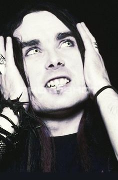 a man with long hair and piercings holding his hands up to his face while looking at the camera