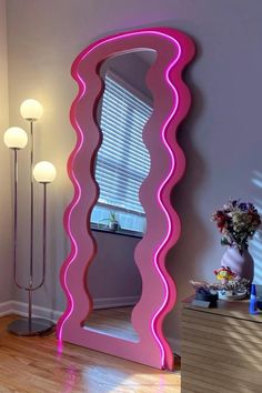 a large pink mirror sitting on top of a wooden floor next to a vase with flowers