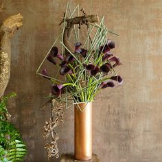 a vase filled with purple flowers sitting on top of a wooden table next to a plant