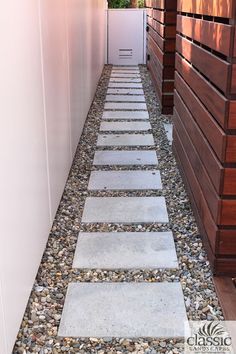 a walkway made out of stones and gravel next to a wooden building with a white door