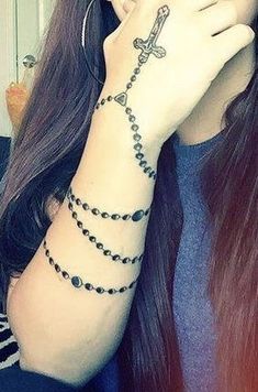 a woman with a rosary tattoo on her arm and hand holding a cell phone up to her face