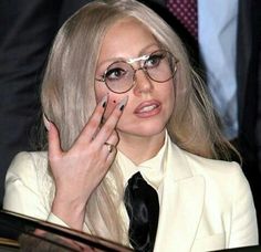 lady in white suit and black tie holding her hand up to her face