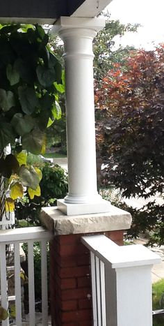 a cat sitting on top of a porch next to a brick wall and white railing