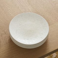 a stack of white plates sitting on top of a wooden table next to a rug