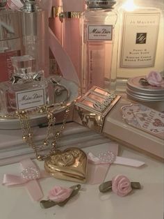 pink perfume bottles and other items on a white counter with gold chains, roses, and hearts