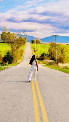 a woman is standing on the side of an empty road with grass and trees in the background