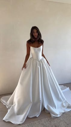 a woman wearing a white wedding dress standing in front of a wall with her hands on her hips