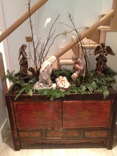 the nativity scene is displayed on top of an old dresser with greenery and figurines