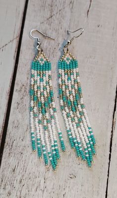 two pairs of beaded earrings on top of a wooden table with white and blue beads